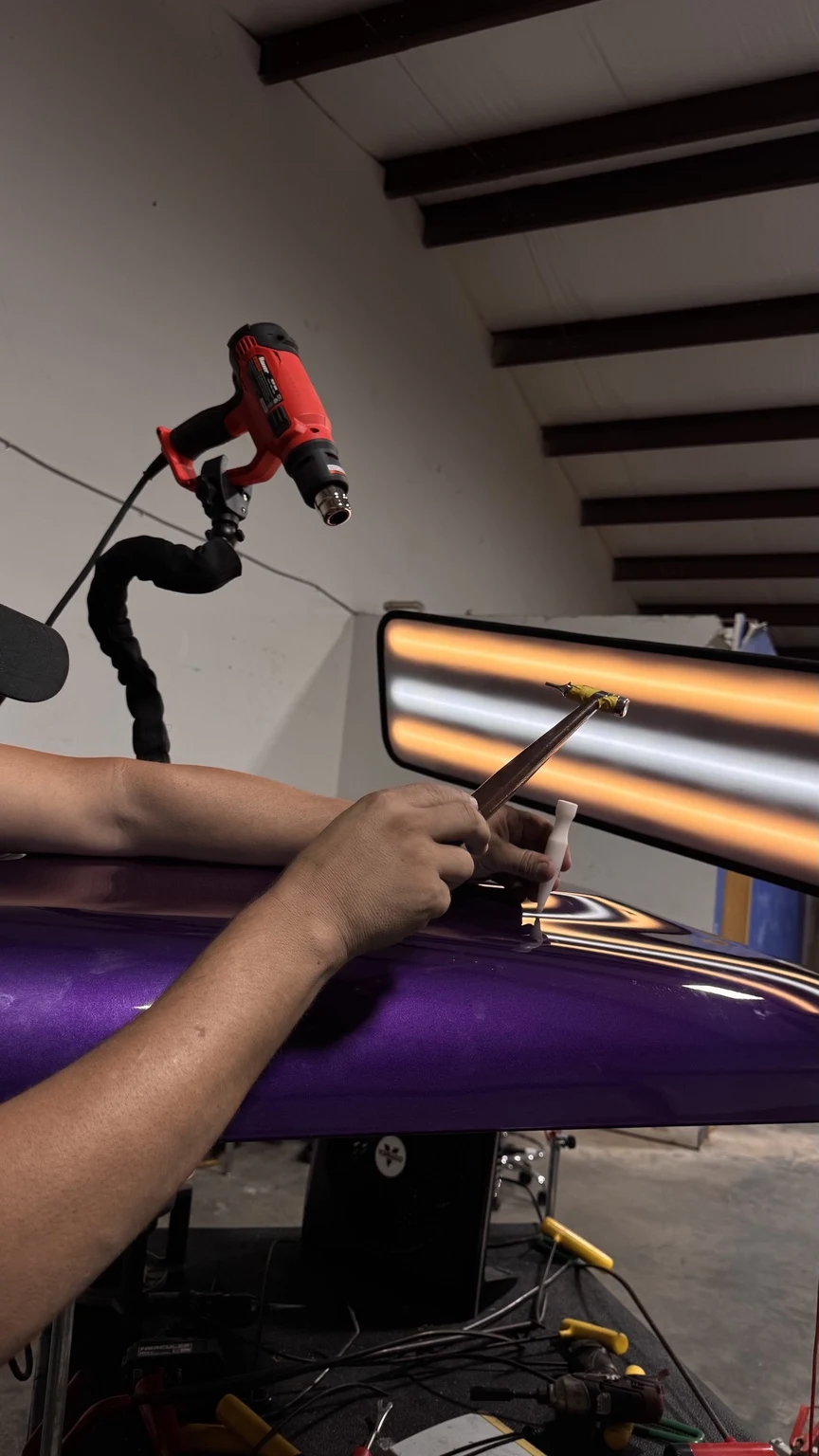Technician repairing a purple hood with paintless dent repair tools